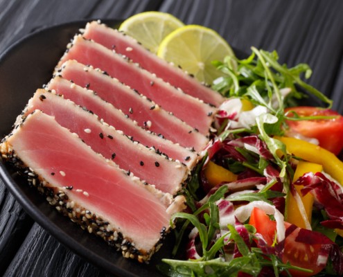 sliced ahi tuna steaks coated in sesame seeds served with lime and salad greens