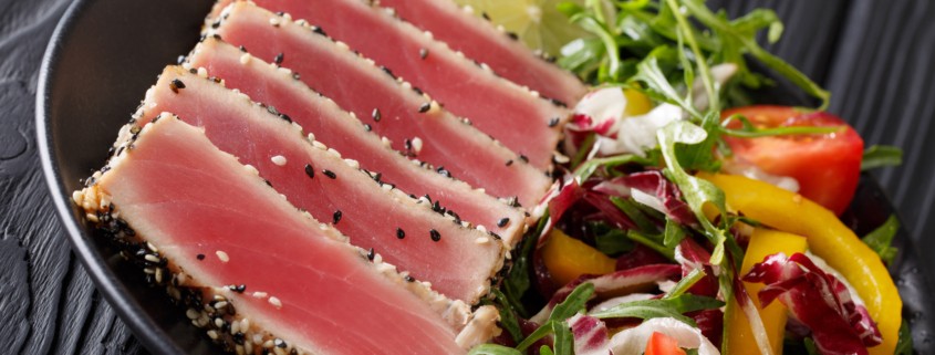 sliced ahi tuna steaks coated in sesame seeds served with lime and salad greens